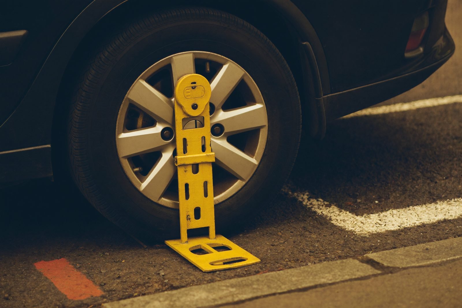 Cepo metálico amarillo inmovilizando la rueda de un vehículo estacionado junto al bordillo